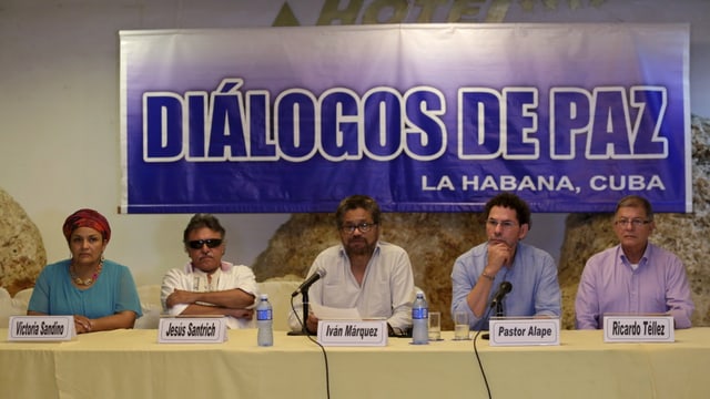 Die Verhandlungsdelegation der Armee und der Farc gibt an einem langen Tisch sitzend die Übereinkunft bekannt. Die Verhandlungsdelegation der Armee und der Farc gibt an einem langen Tisch sitzend die Übereinkunft bekannt.