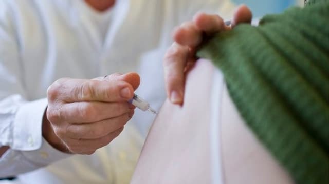 Ein Mann verabreicht einer Frau eine Impfung in den Oberarm.