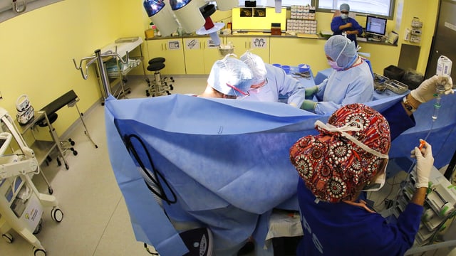 Blick in einen Operationssaal. Hinter einem Tuch steht der Anästhesist. Vor dem Tuch wird operiert.