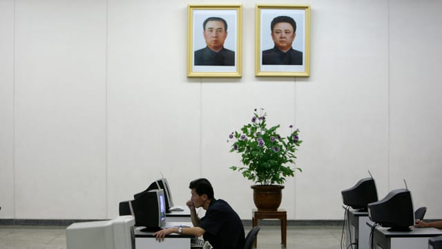 Ein Nordkoreaner sitzt an einem Computer, über ihm an die Wand gehängt ein Portrait von Kim Il-sun und Kim Jong-il. Ein Nordkoreaner sitzt an einem Computer, über ihm an die Wand gehängt ein Portrait von Kim Il-sun und Kim Jong-il.