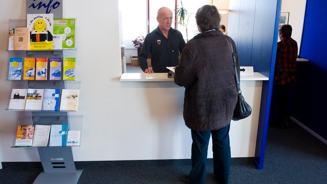 Frau steht an einem Schalter der Arbeitslosenversicherung Frau steht an einem Schalter der Arbeitslosenversicherung