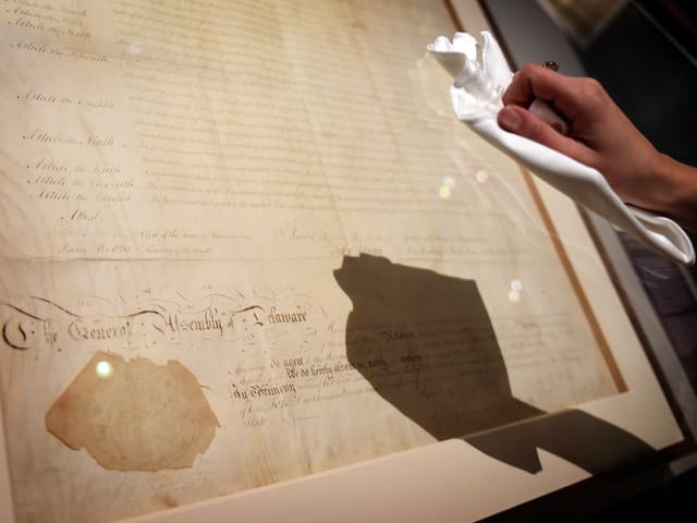 Eine Hand putzt mit einem Lumpen ein wertvolles Stück Papier, geschützt hinter Glas. Eine Hand putzt mit einem Lumpen ein wertvolles Stück Papier, geschützt hinter Glas.