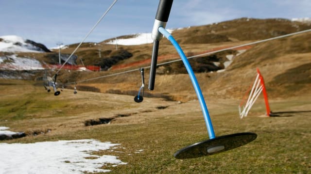 Ein Skilift-Teller im Vordergrund. Im Hintergrudn eine grüne Wiese mit etwas Schnee. Ein Skilift-Teller im Vordergrund. Im Hintergrudn eine grüne Wiese mit etwas Schnee.