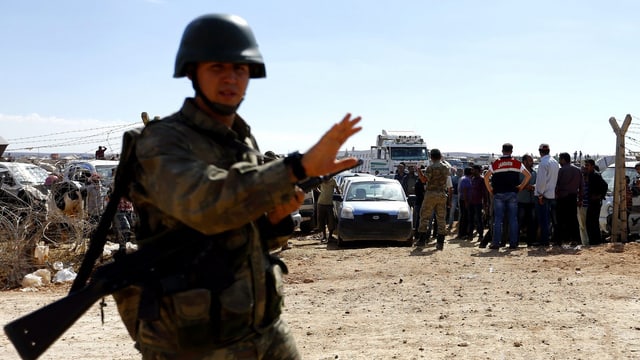 Türkischer Soldat, dahinter Flüchtlinge. Türkischer Soldat, dahinter Flüchtlinge.