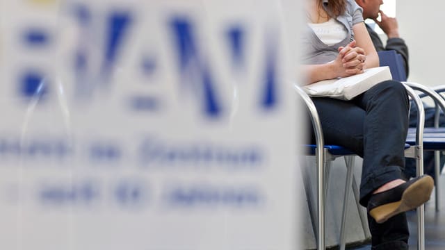 Ein verschwommenes Schild des RAV. Hintergrund sitzt eine Frau. Ein verschwommenes Schild des RAV. Hintergrund sitzt eine Frau.