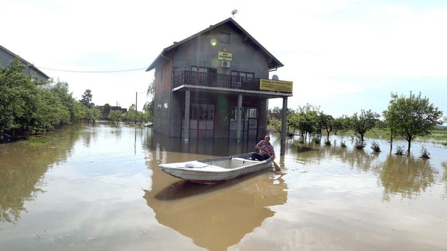 Haus, völlig vom Wasser eingeschlossen. Davor ein Mann in einem Boot. Haus, völlig vom Wasser eingeschlossen. Davor ein Mann in einem Boot.