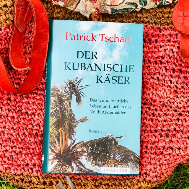 Der Schelmenroman «Der kubanische Käser» von Patrick Tschan liegt auf einer Beuteltasche Der Schelmenroman «Der kubanische Käser» von Patrick Tschan liegt auf einer Beuteltasche