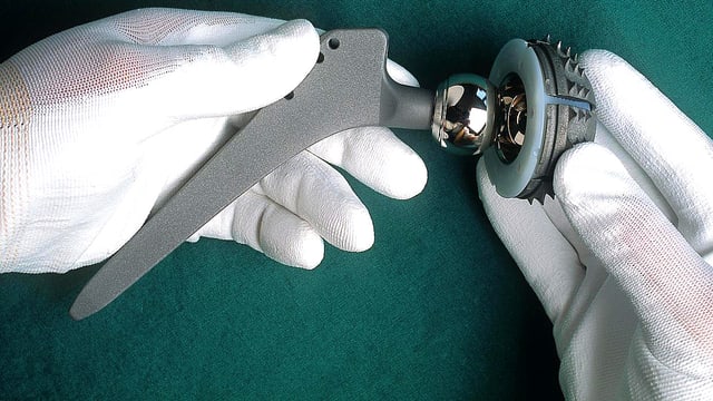 Aufnahme zweier Technikerhände, die ein künstliches Hüftgelenk der Firma Sulzer halten.