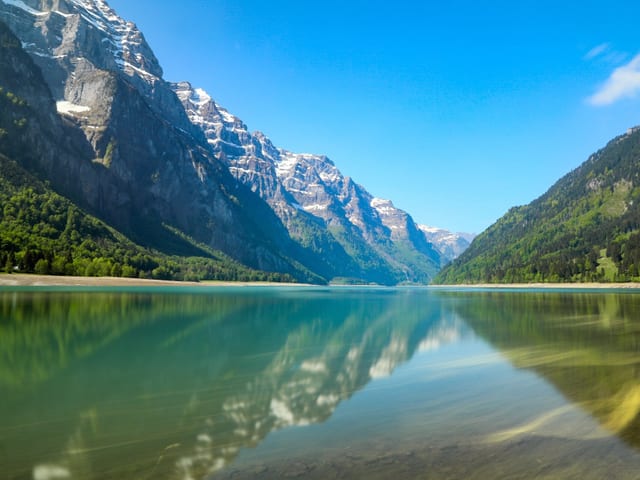 See mit türkis farbenem Wasser und Bergkulisse.