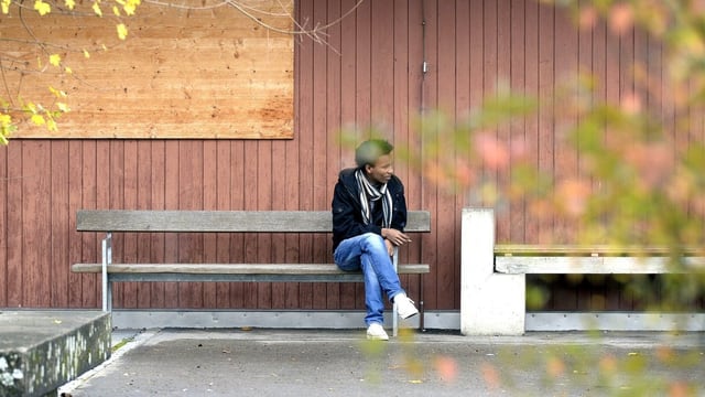 Ein Mann sitzt auf einer Bank vor einer Holzhütte.