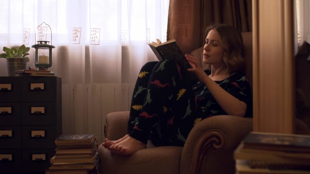 eine junge Frau sitzt im Pyjama auf einem Sessel und liest eine junge Frau sitzt im Pyjama auf einem Sessel und liest
