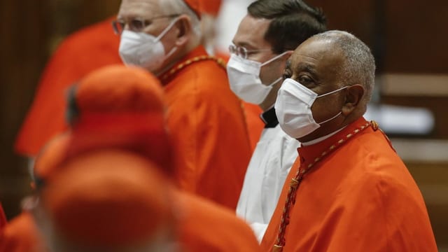 Dark man in red robe and with protective mask.