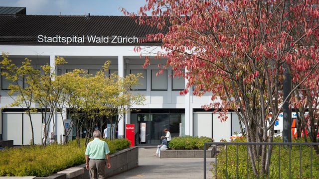 Aussenansicht des Stadtspitals Waid. Ein älterer Mann läuft an einem Baum vorbei zum Eingang. Aussenansicht des Stadtspitals Waid. Ein älterer Mann läuft an einem Baum vorbei zum Eingang.