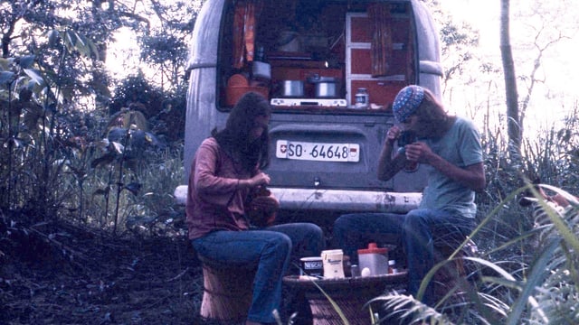 Ein junges Paar isst zusammen vor dem VW-Bus im Wald. Ein junges Paar isst zusammen vor dem VW-Bus im Wald.