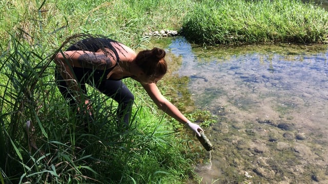 Eine junge Frau fischt eine Aludose aus dem Wasser
