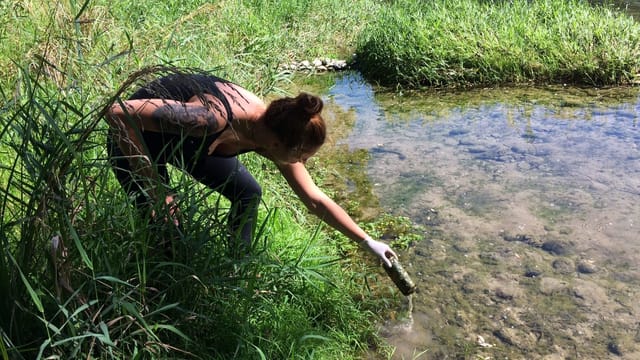 Eine junge Frau fischt eine Aludose aus dem Wasser Eine junge Frau fischt eine Aludose aus dem Wasser