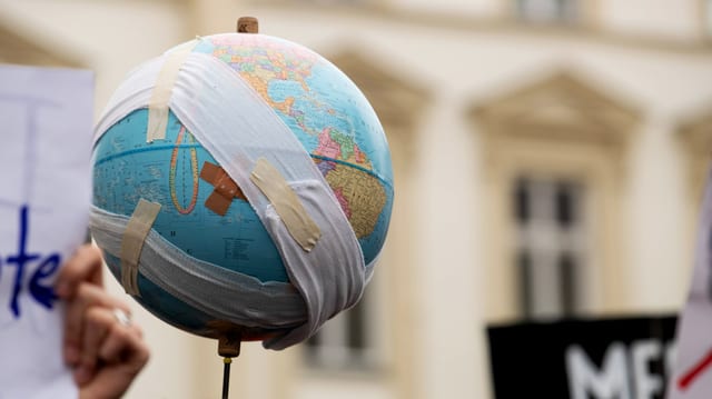 Eine Erdball mit Pflastern wird bei einer Demo in die Luft gehalten. Eine Erdball mit Pflastern wird bei einer Demo in die Luft gehalten.