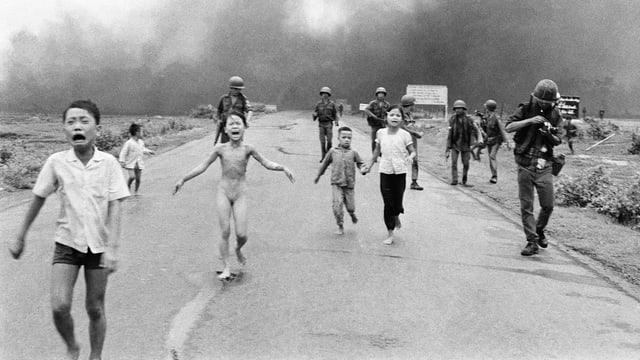 Kinder rennen weinend eine Strasse hinunter, hinter ihnen Rauch und Soldaten. Kinder rennen weinend eine Strasse hinunter, hinter ihnen Rauch und Soldaten.