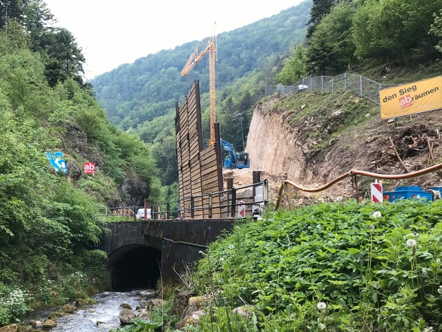Bach fliesst in Röhre unter Strasse. Daneben Baustelle. Bach fliesst in Röhre unter Strasse. Daneben Baustelle.