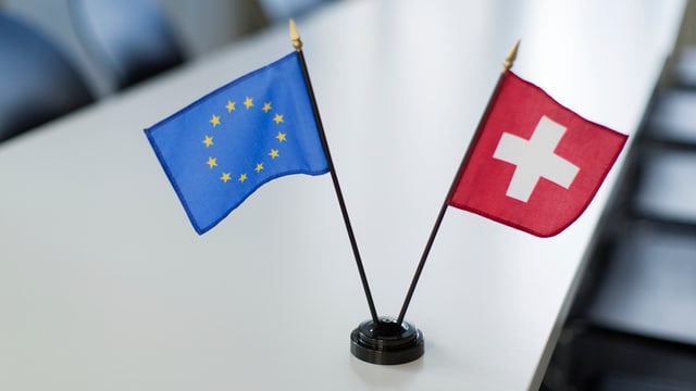 Die Flaggen der EU und der Schweiz stehen im Miniatur-Format auf einem Konferenztisch. Die Flaggen der EU und der Schweiz stehen im Miniatur-Format auf einem Konferenztisch.