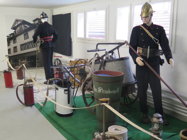 Löscheimer, Löschschläuche und zwei Puppen in alter Feuerwehruniform.