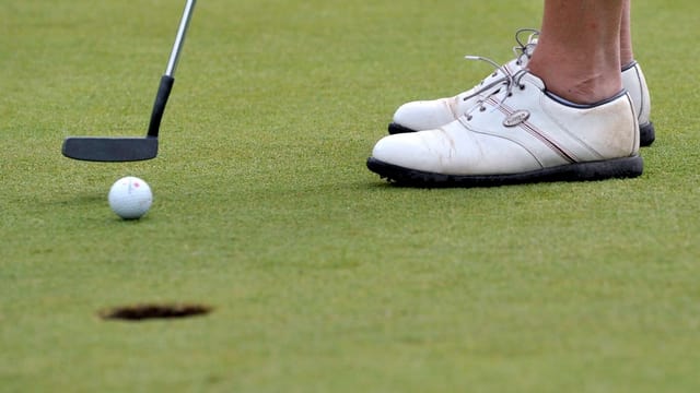Ein Golfball steht wenige Zentimeter vor einem Golfloch. Ein Golfball steht wenige Zentimeter vor einem Golfloch.