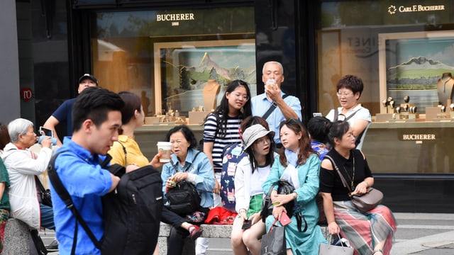 Eine Gruppe asiatischer Touristen sitzt vor den Schaufenstern eines Uhrengeschäfts Eine Gruppe asiatischer Touristen sitzt vor den Schaufenstern eines Uhrengeschäfts