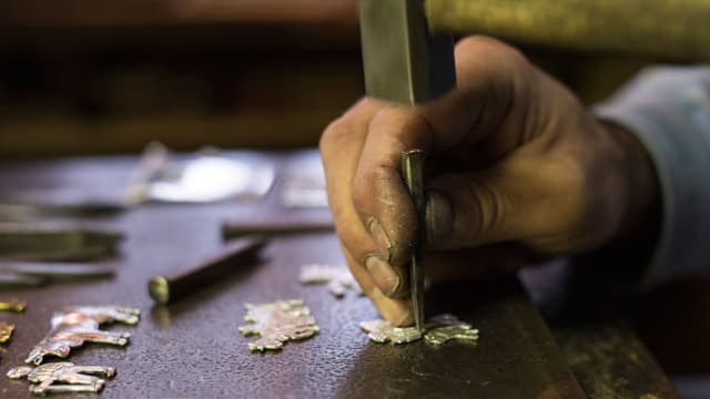 EIne Hand beim kunstvollen Bearbeiten von eines Messingbeschlags. EIne Hand beim kunstvollen Bearbeiten von eines Messingbeschlags.