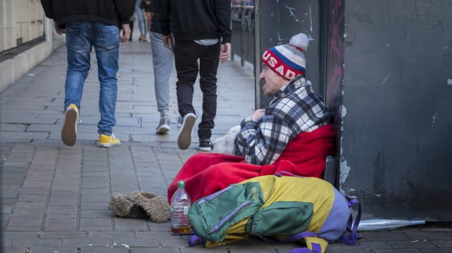 Bettler sitzt auf Trottoir, Leute gehen an ihm vorbei Bettler sitzt auf Trottoir, Leute gehen an ihm vorbei