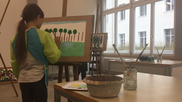 Ein Mädchen malt an einer Staffelei ein Bild.