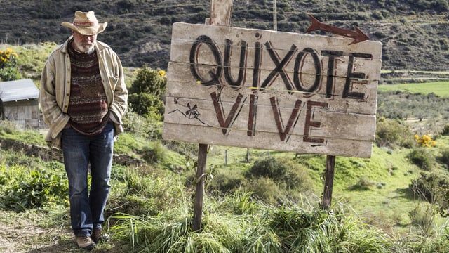 Mann neben einem Schild mit der Aufschrift "Quixote vive" Mann neben einem Schild mit der Aufschrift "Quixote vive"