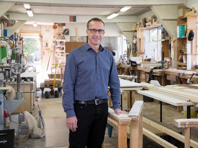 Ein Mann mit blauem Hemd steht in der Werkstatt einer Schreinerei. Ein Mann mit blauem Hemd steht in der Werkstatt einer Schreinerei.
