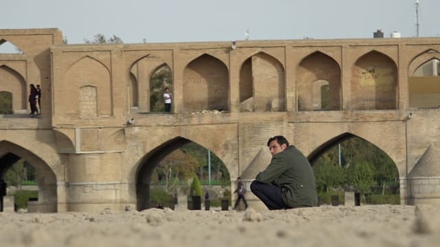 Mann sitzt in Isfahan, Iran in der Nähe einer Brücke.