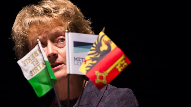 Eveline Widmer-Schlumpf vor drei kleinen Fähnchen (Genf, Waadt und noch eines) an einem Rednerpult. Eveline Widmer-Schlumpf vor drei kleinen Fähnchen (Genf, Waadt und noch eines) an einem Rednerpult.