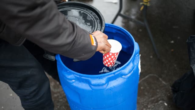 Eine Hand schöpft Wasser mit einem Becher aus einem blauen Kanister. Eine Hand schöpft Wasser mit einem Becher aus einem blauen Kanister.
