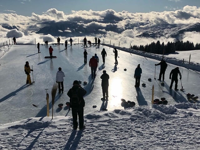 Natureisfeld in den Bergen mit Menschen die Curling spielen und schlittschuhlaufen.