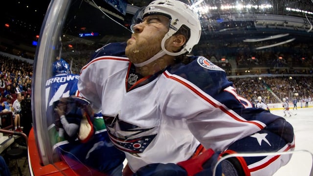 Ein Eishockeyspieler mit weissem Helm, der sich sein Gesicht an der Bande flachdrückt. Ein Eishockeyspieler mit weissem Helm, der sich sein Gesicht an der Bande flachdrückt.