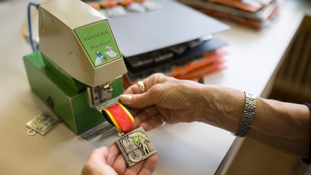 Ein Arbeiter (nur die Hände sichtbar) prägt ein Abzeichen für ein Feldschiessen. Ein Arbeiter (nur die Hände sichtbar) prägt ein Abzeichen für ein Feldschiessen.