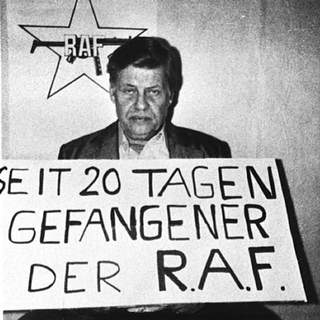 Hanns Martin Schleyer hät ein Plakat vor sich auf dem steht: «Seit 20 Tagen Gefangener der RAF». Im Hintergrund ist das Logo der RAF. Hanns Martin Schleyer hät ein Plakat vor sich auf dem steht: «Seit 20 Tagen Gefangener der RAF». Im Hintergrund ist das Logo der RAF.