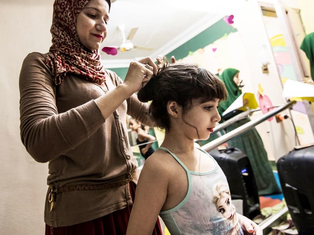 Eine Mutter macht einem Kind die Haare. Es trägt ein Tutu und Make-up. Eine Mutter macht einem Kind die Haare. Es trägt ein Tutu und Make-up.