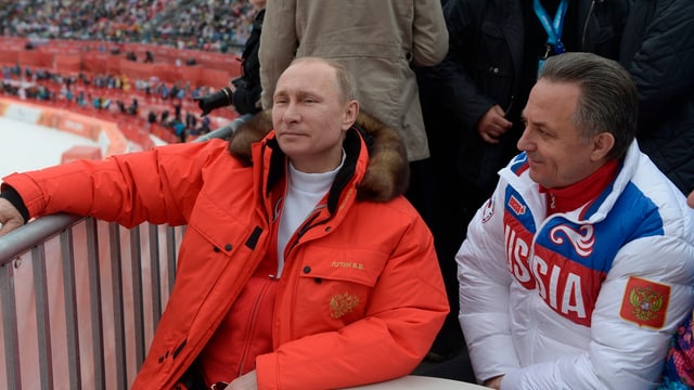 Waldimir Putin (links) sitzt in Winterjacke neben Witali Mutko (rechts) in Winterjacke.