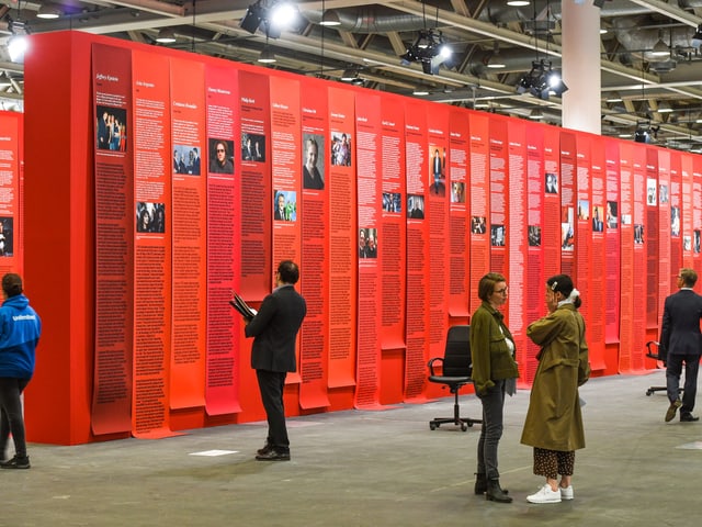 Menschen stehen vor einer roten Wand mit Texten Menschen stehen vor einer roten Wand mit Texten