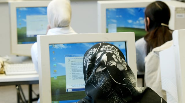 Frauen mit Kopftüchern von hinten, sitzen an Computern, daneben eine Frau ohne Kopftuch Frauen mit Kopftüchern von hinten, sitzen an Computern, daneben eine Frau ohne Kopftuch