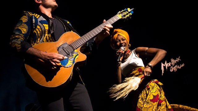 Ein Mann mit Gitarre und eine Frau in afrikanischer Tracht auf der Bühne. Ein Mann mit Gitarre und eine Frau in afrikanischer Tracht auf der Bühne.