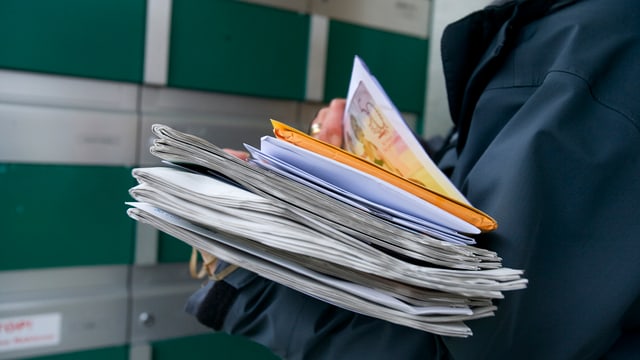 Ein Briefträger verteilt Post in einen Briefkasten bei einem Mehrfamilienhaus. Ein Briefträger verteilt Post in einen Briefkasten bei einem Mehrfamilienhaus.