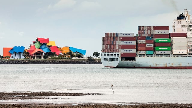 Das bunte Museum im Hintergrund, davor die Wasserstrasse, auf der ein Containerschiff fährt. Das bunte Museum im Hintergrund, davor die Wasserstrasse, auf der ein Containerschiff fährt.