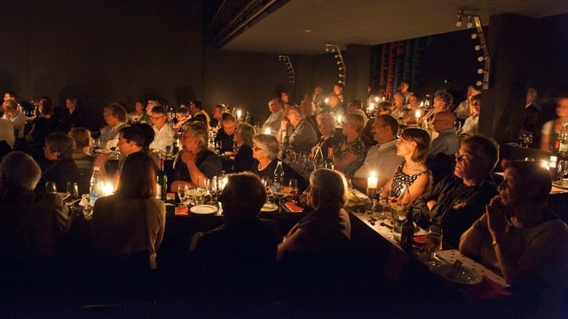 Viele Menschen sitzen in einem Saal an vielen kleinen Tischen und essen Viele Menschen sitzen in einem Saal an vielen kleinen Tischen und essen