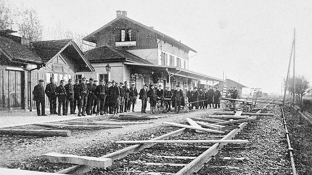 Mehrere Männer stehen an einem Bahnhof Mehrere Männer stehen an einem Bahnhof