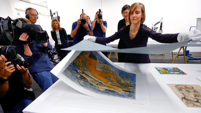 Eine Frau hebt ein Deckblatt von einer Zeichnung ab. Pressefotografen fotografieren. Eine Frau hebt ein Deckblatt von einer Zeichnung ab. Pressefotografen fotografieren.