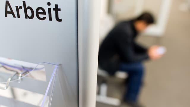 Schriftzug «Abeit», daneben ein sitzender Mann. Schriftzug «Abeit», daneben ein sitzender Mann.